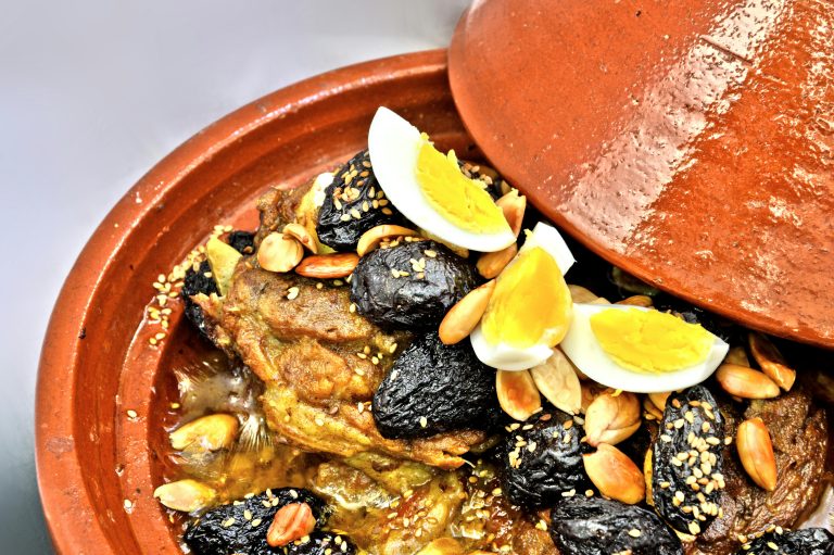 Plate of traditional Moroccan couscous garnished with vegetables and chickpeas, served with a side of mint tea